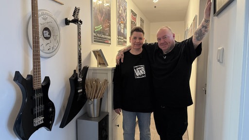 Ein Mann und eine Frau stehen in einem Flur. An der Wand hängen Instrumente.