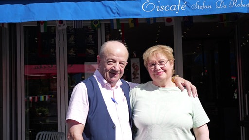 Ein Mann und eine Frau posieren vor einem Café. Die Markise liest "Eiscafé Stefan da Roberto"
