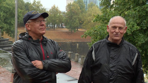 Zwei Männer stehen mit Regenjacken im Regen