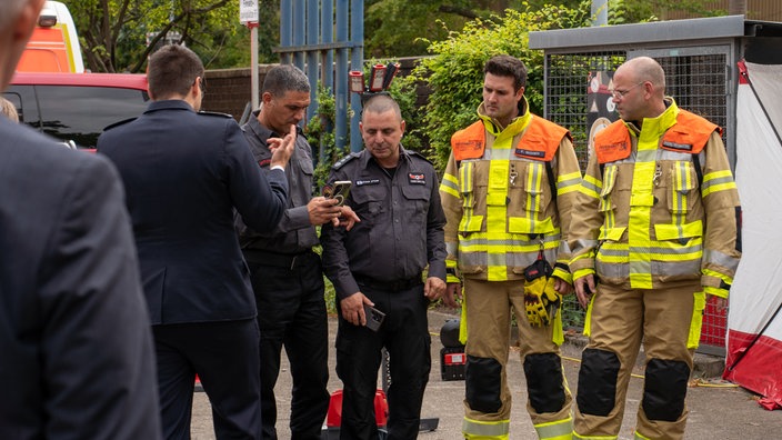Shiran Luzon und Shmulik Amsalem stehen zusammen mit Ausbildern der Düsseldorfer Feuerwehrschule und diskutieren.