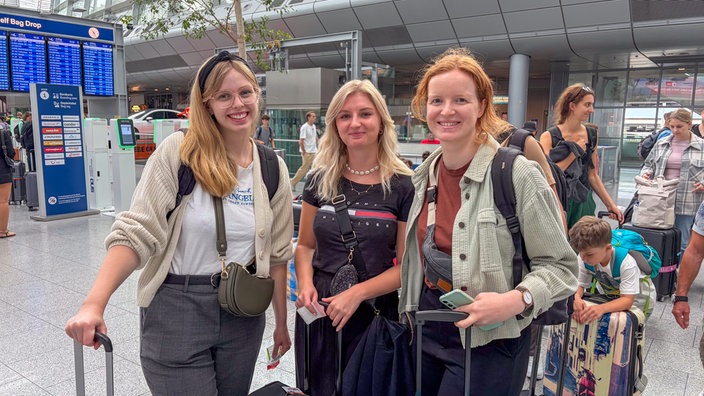 Drei junge Frauen stehen am Flughafen Düsseldorf in der Warteschlange.