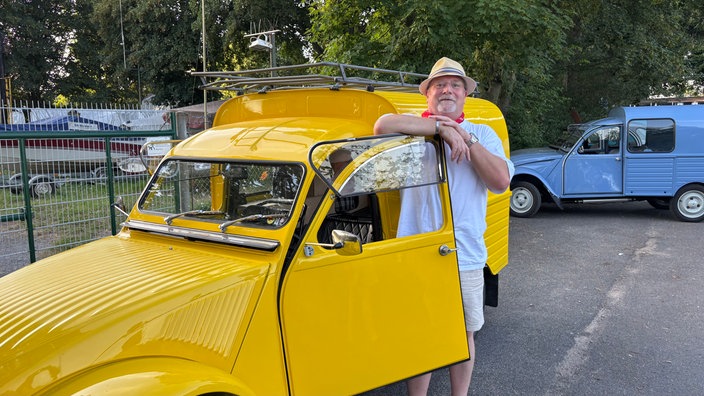 Ein Mann steht vor einem gelben Auto, Modell "Ente" von Citroen