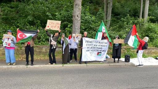 Protestierende stehen mit Plakaten vor einem Turniergelände