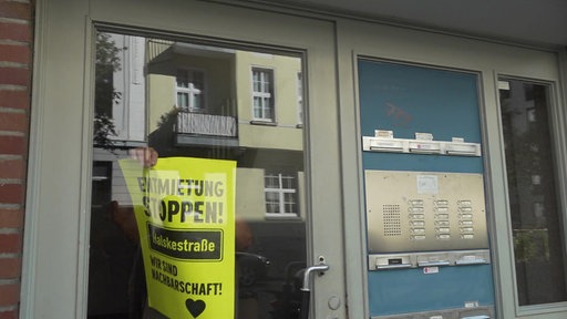 Eine Haustür, dahinter bringt jemand ein neongelbes Plakat am Fenster an mit der Aufschrift: "Entmietung stoppen"