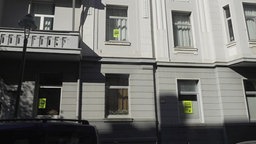 Ein Haus von außen, in mehrern Fenstern hängen Neongelbe Plakate mit der Aufschrift "Entmietung stoppen!"