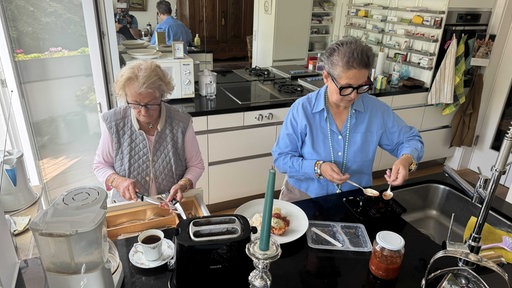 Zwei Frauen stehen in einer Küche und kochen. 