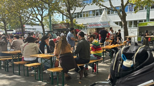 An Bierbänken sitzen Menschen vor Food Trucks