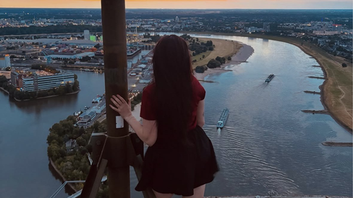 Die Influencerin posiert oben auf dem Rheinturm. Sie ist von hinten zu sehen. Im Hintergrund ist der Blick über den Rhein zu sehen.