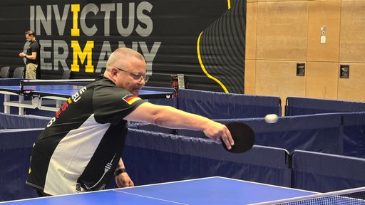 Mittelältriger Mann spielt Tischtennis, Trikot hat eine Deutsche Flagge