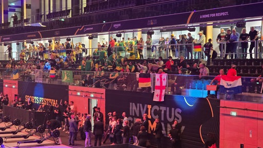 Tribühne voller Menschen mit verschiedenen Flaggen. Beschriftung liest "Invictus Germany" und "Invictus Festival"