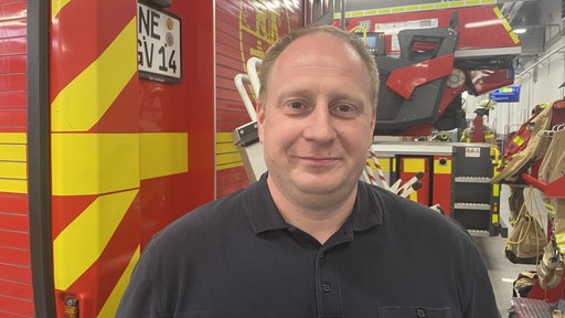 Ein Mann steht in vor einem Feuerwehr Auto und schaut in die Kamera