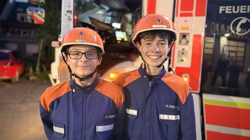 Clemens und Niklas von der Jugendfeuerwehr stehen vor einem Löschfahrzeug.