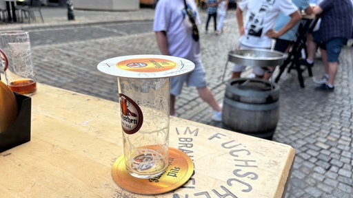 Ein leeres Alt-Glas steht auf einem Tisch in einem Brauhaus. Das Glas ist mit einem Bierdeckel abgedeckt.