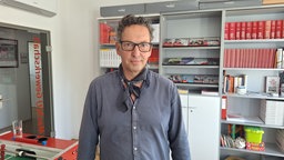 Ein Mann, der ein graues Hemd trägt, steht in seinem Büro.