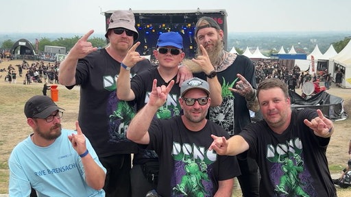 Sechs Männer posieren vor einer Festivalbühne