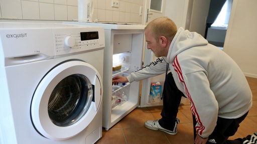 Ein Mann greift in den Kühlschrank, links daneben steht eine Waschmaschine
