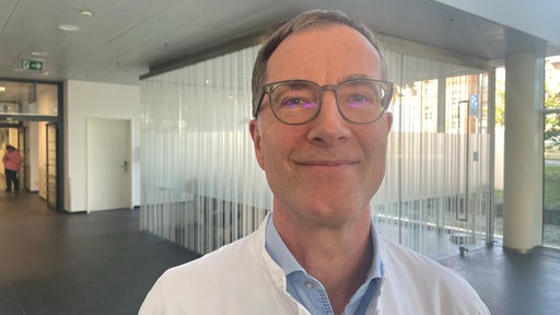 Auf dem Bild sieht man einen Mann im Universitätsklinikum Düsseldorf, der in die Kamera lächet, der Mann heißt Thorsten Feldt