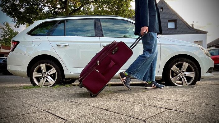 Eine Frau zieht ihren Koffer und geht an einem Auto vorbei