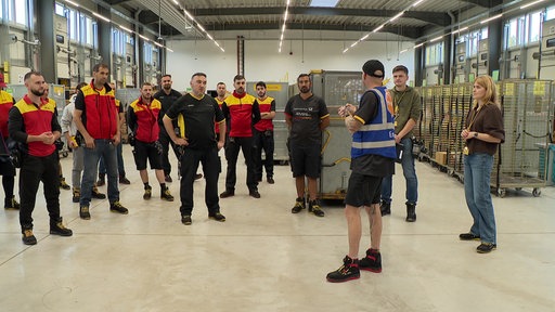 Paketzusteller in einer Halle während sie von einem Trainer gebrieft werden
