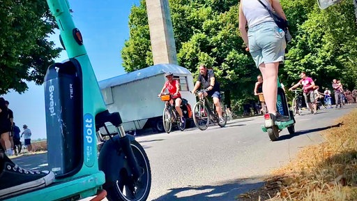 Menschen fahren mit Fahrrädern und E-Scootern über einen Weg.