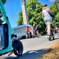 Menschen fahren mit Fahrrädern und E-Scootern über einen Weg.