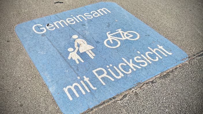 Ein Schild auf einem Boden zeigt Fußgänger und ein Fahrrad