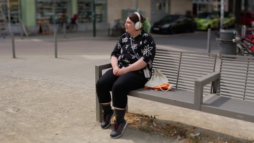 Can sitzt auf einer Parkbank und hört Musik.
