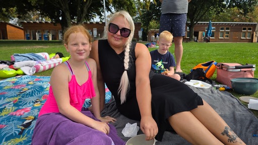 Marina und Tochter Lea aus Kaarst genießen noch mal die Sonne. Sie liegen auf einer grünen Wiese im Freibad.
