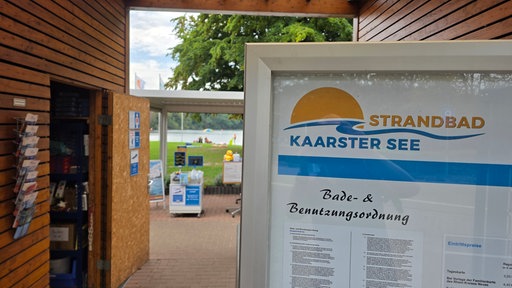 Zu sehen ist der Eingang zum Strandbad Kaarster See, das in diesem Jahr sehr gut besucht war. Rechts ist ein Schild zu sehen, im Hintergrund der See.