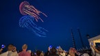 Zwei Quallen bei der Drohnenshow der Rheinkirmes, im Vordergrund Zuschauer mit Handys