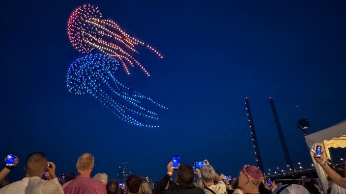 Zwei Quallen bei der Drohnenshow der Rheinkirmes, im Vordergrund Zuschauer mit Handys