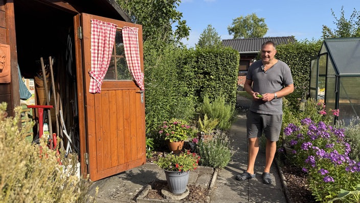 Ein Mann steht in einem Garten neben seiner Hütte.
