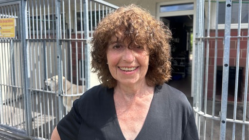 Winnie Bürger, Vorsitzende vom Tierschutzverein in Düsseldorf-Rath, ist im Porträt zu sehen. Sie steht vor einigen Hundezwingern.