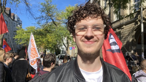Ein junger Mann steht zwischen anderen Streik-Teilnehmern auf einer Straße.