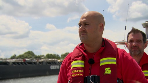 Florian Droß steht in seinen roten Einsatzklamotten auf dem Boot und blickt in die Ferne.