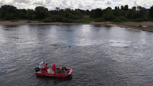 Ein Rettungsboot der DLRG treibt auf dem Rhein, die Wasserretter haben zwei Schwimmer im Blick, die versuchen, gegen die Strömung zu schwimmen.