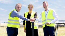 Jochen Kral, Beigeordneter der Landeshauptstadt Düsseldorf, Mona Neubaur, NRW-Klimaschutzministerin und Lars Redeligx, Düsseldorfer Flughafenchef, drücken gemeinsam auf einen roten Knopf.