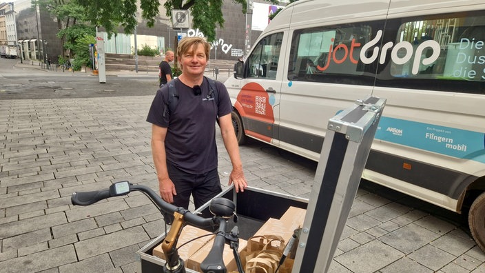 Thomas Tackenberg steht vor einem Transporter und stützt sich auf ein Lastenrad, in dem Pakete liegen.