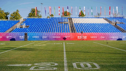Die Bezirksportanlage in Düsseldorf-Garath. Hier noch bereit für die Flag Football World Championships: Auf dem Rasen sind Markierungen für Football zu sehen. Im Hintergrund Tribünen mit blauen Sitzen.