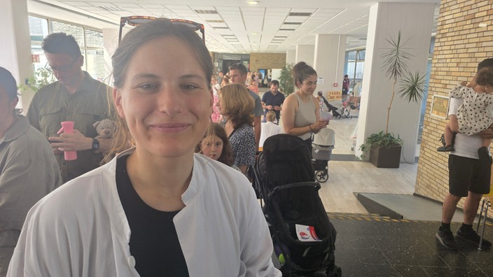Ein Frau im Arztkittel und Sonnenbrille im Haar inmitten vieler Eltern mit Kindern