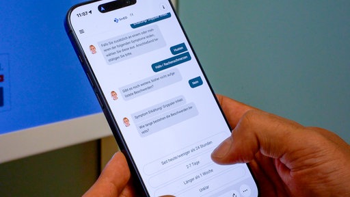Auf einem Handy ist ein Chatverlauf zu sehen, bei dem abgefragt wird, welche Beschwerden der Patient hat und wie lange schon.