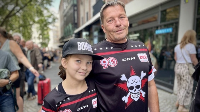 Vater und Tochter stehen Arm in Arm in der Düsseldorfer Innenstadt. Sie tragen ein Fan-Shirt der Toten Hosen.