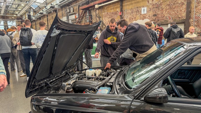 Mehrere Menschen stehten über dem geöffneten Motorraum eines Autos