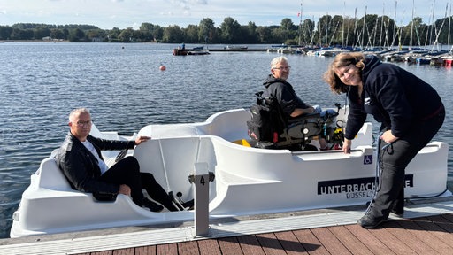 Mann im Rollstuhl auf Boot mit Pflegern