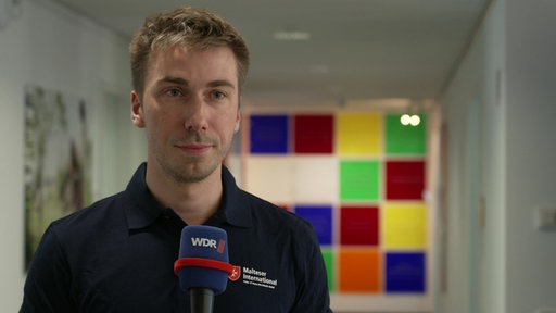 Ein junger Mann mit Drei-Tage-Bart und dunklem Polo-Shirt in einem Gang