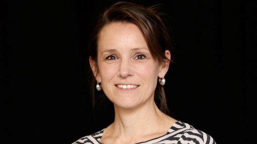 Eine Frau im Portrait vor einem schwarzen Hintergrund.