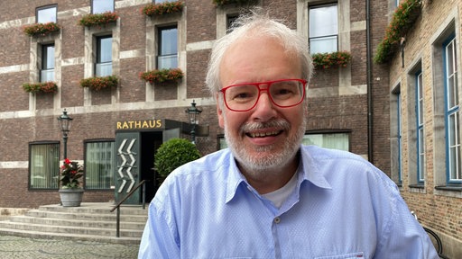 Ein Mann mit roter Brille und blauem Hemd steht vor dem düsseldorfer Rathaus