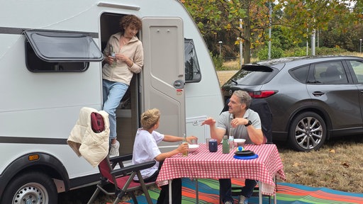 Eine Familie sitzt draußen an einem Camper-Tisch