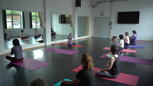 Yogalehrerin Kunie Baba gibt in einem Kursraum Yogaunterricht. Es sind auch weitere Frauen zu sehen, die mitmachen.