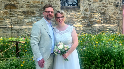 Sascha Fitting und Miriam Uehren aus Bochum stehen in Hochzeitskleidung vor einer Kirche.